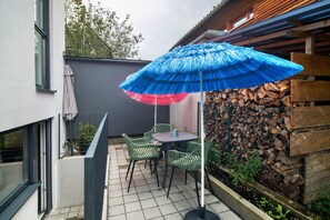 A patio with a table and chairs, a blue umbrella, and a stack of firewood.
