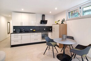Une cuisine moderne avec des meubles blancs, un plan de travail noir et un coin repas comprenant deux chaises et une table.