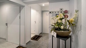 Un couloir avec une pancarte de bienvenue, une plante en pot et un paillasson.