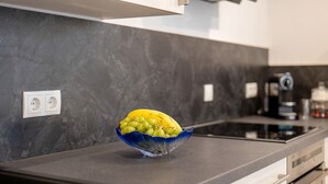 Une cuisine au design moderne, dotée d’un pare-feu en marbre, d’un four encastré et d’un plan de travail sur lequel se trouve un panier de fruits contenant des raisins et une banane.