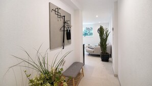 Un couloir avec un banc, un porte-manteau fixé au mur et une plante en pot.