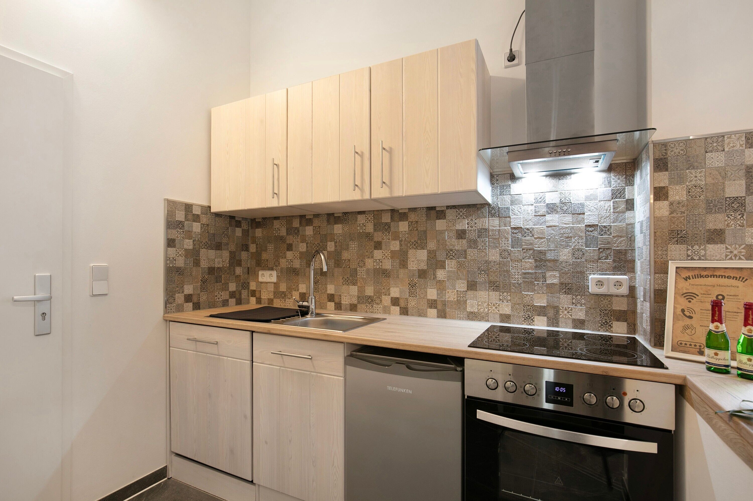 Une cuisine compacte avec des meubles de couleur bois clair, une cuisinière à gaz moderne et un lave-vaisselle.