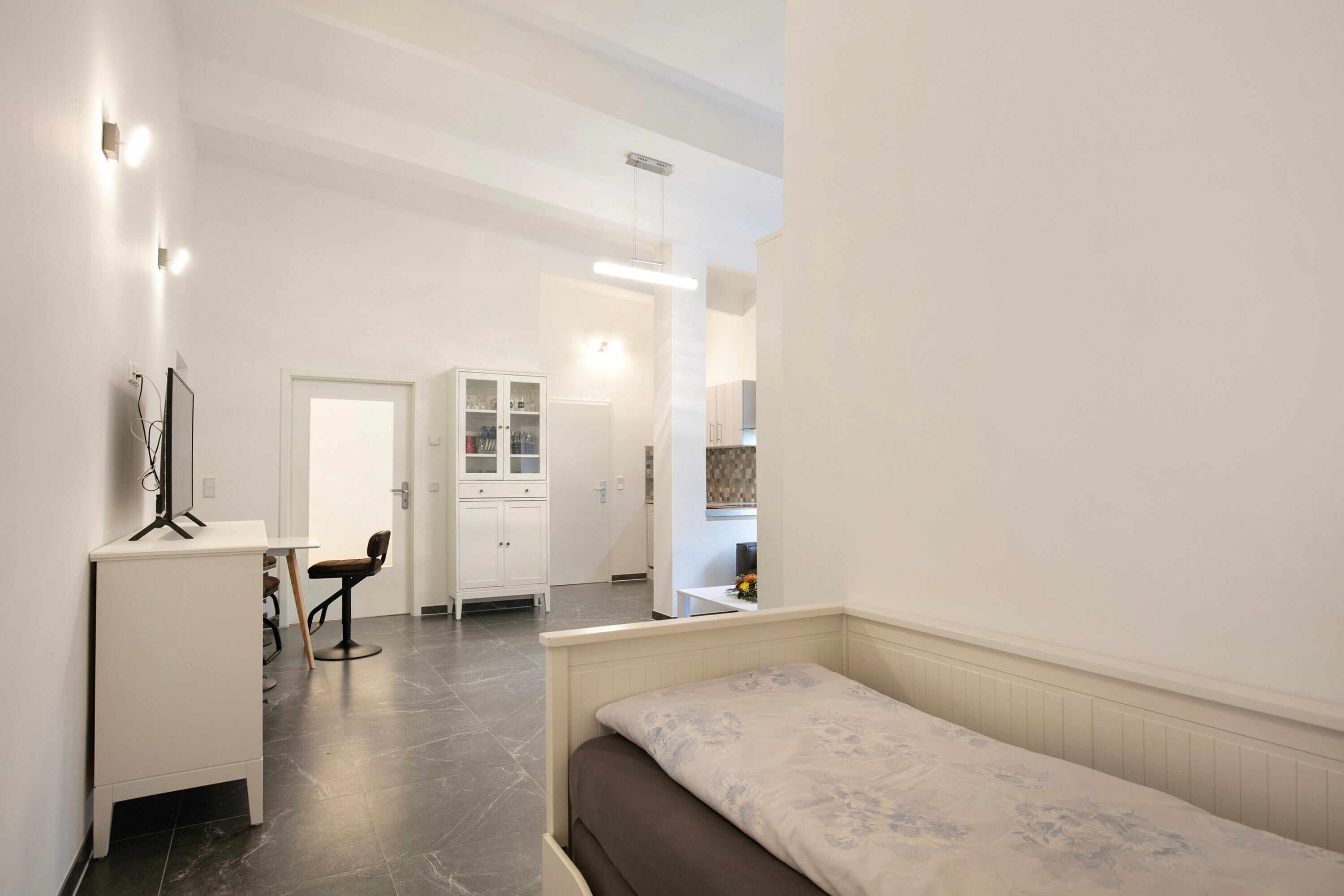 A bedroom with a bed, a desk, a chair, a wardrobe, and a bathroom visible in the background.