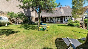 A courtyard with a lawn, a play area with a toy tractor, and a traditional building with exposed wooden beams. - Holiday Home 'Ferienhäuschen Kleine Auszeit' with Private Terrace, Private Garden and Wi-Fi (Seesbach)