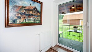 Ein Zimmer mit einem großen Gemälde eines Gebäudes, einem Heizkörper und Blick durch eine Glastür auf einen Außenbereich mit Tisch und Pflanze.