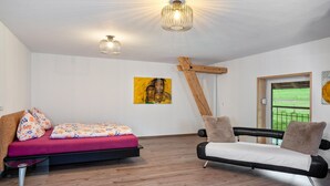 Ein Zimmer mit einem Bett, einer Schlafcouch, sichtbaren Holzbalken und einem Fenster mit Blick.