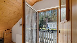 Une pièce avec un plafond en bois, une porte-fenêtre coulissante donnant sur un balcon, un radiateur et une petite table.
