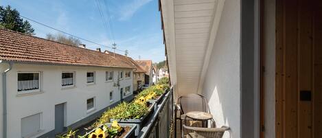 Un balcone con un filare di girasoli, una sedia in vimini e una porta in legno.