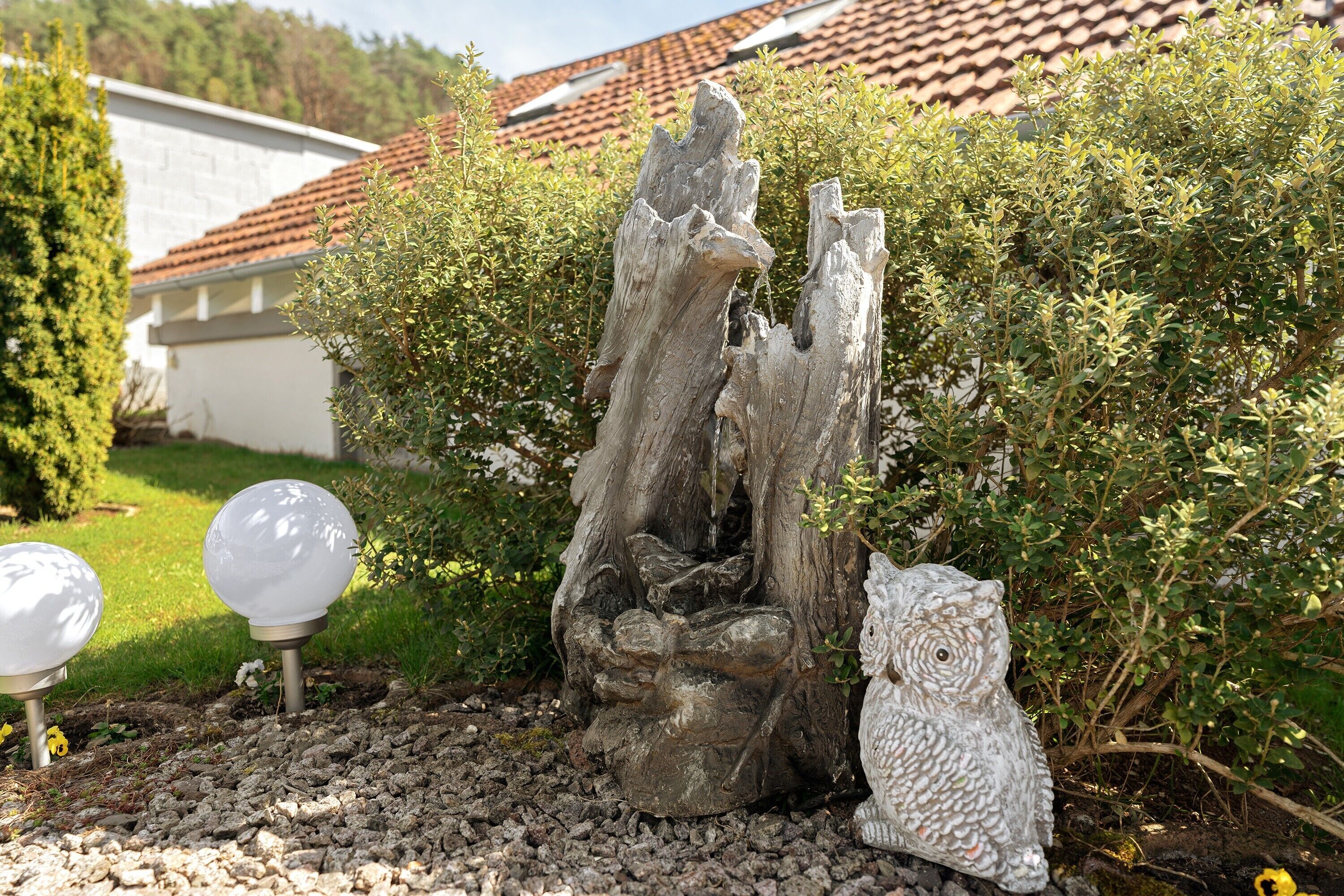 En have med en træskulptur, en hvid uglefigur og sfæriske lys.