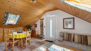 Une pièce mansardée chaleureuse avec un plafond en bois, une table à manger avec des chaises, un canapé, un petit banc et une porte donnant sur une autre pièce.