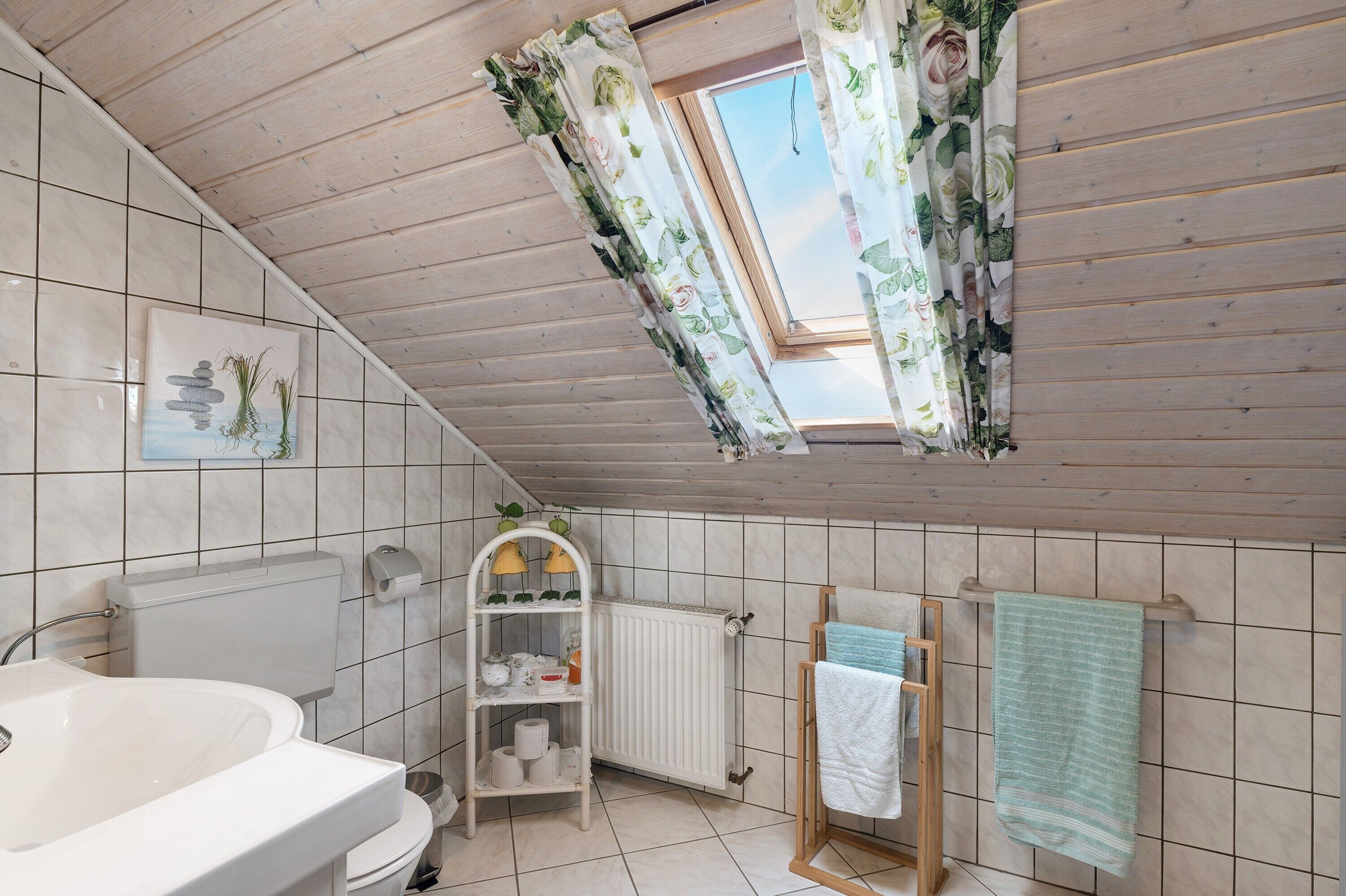 A bathroom with a skylight, a white toilet, a sink, a towel rack, and a shelf with toiletries.