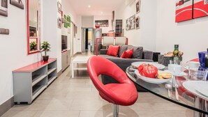 Una sala de estar moderna con una silla roja, una mesa de comedor con platos y cubiertos, y un sofá con cojines rojos.