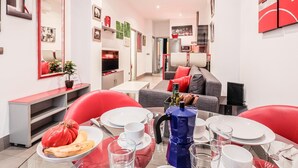 Una sala moderna con comedor, que incluye un sofá, sillas rojas, una mesa de centro y una cocina al fondo.