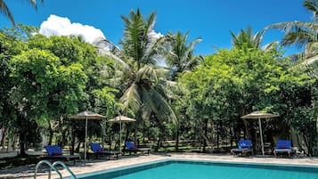 Une piscine entourée d’une végétation luxuriante et de palmiers, avec des chaises longues et des parasols à proximité.