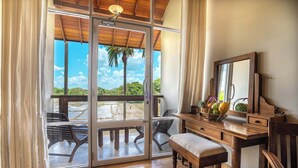 A room with a wooden desk, a bench, and a large window with a view of a palm tree and a water body. - Lavendish Wild Wilpattu (Nochchiyagama)