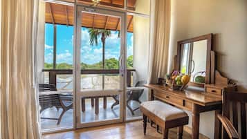 Una habitación con un escritorio de madera, un banco y un ventanal con vistas a una palmera y un cuerpo de agua.