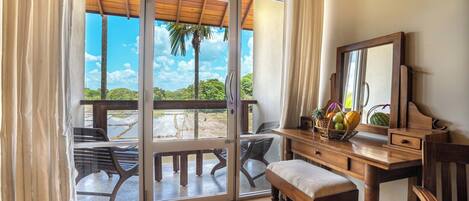 A room with a wooden desk, a bench, and a large window with a view of a palm tree and a water body.