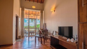 Una habitació àmplia amb terra de fusta, una televisió sobre un suport de fusta i un gran finestral amb vista a l'exterior.