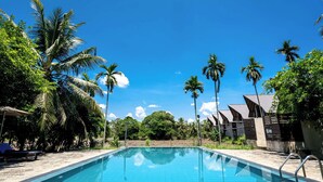 A swimming pool surrounded by palm trees and a building with a sloped roof. - Lavendish Wild Wilpattu (Nochchiyagama)