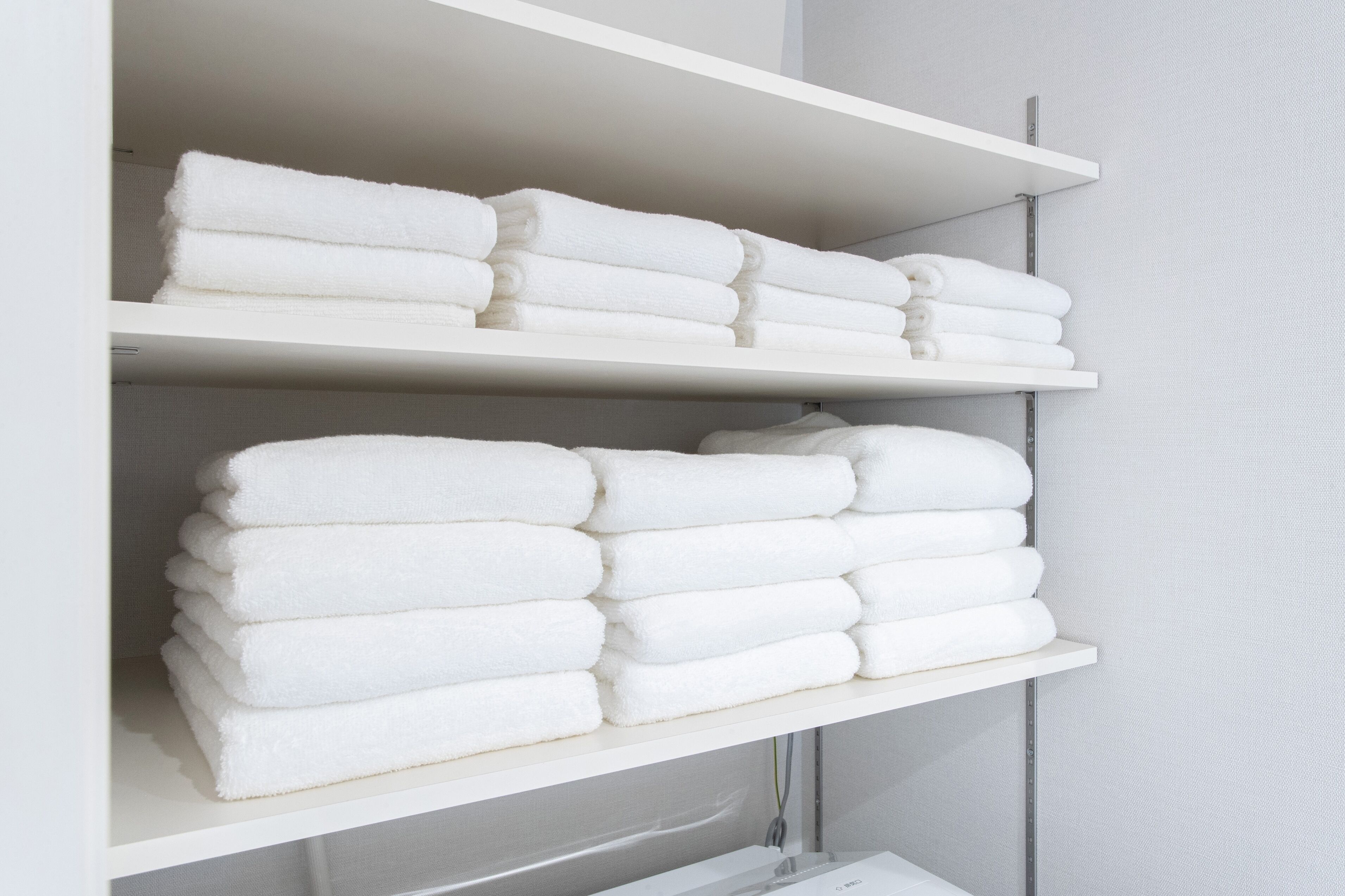 A white shelf with neatly folded white towels.