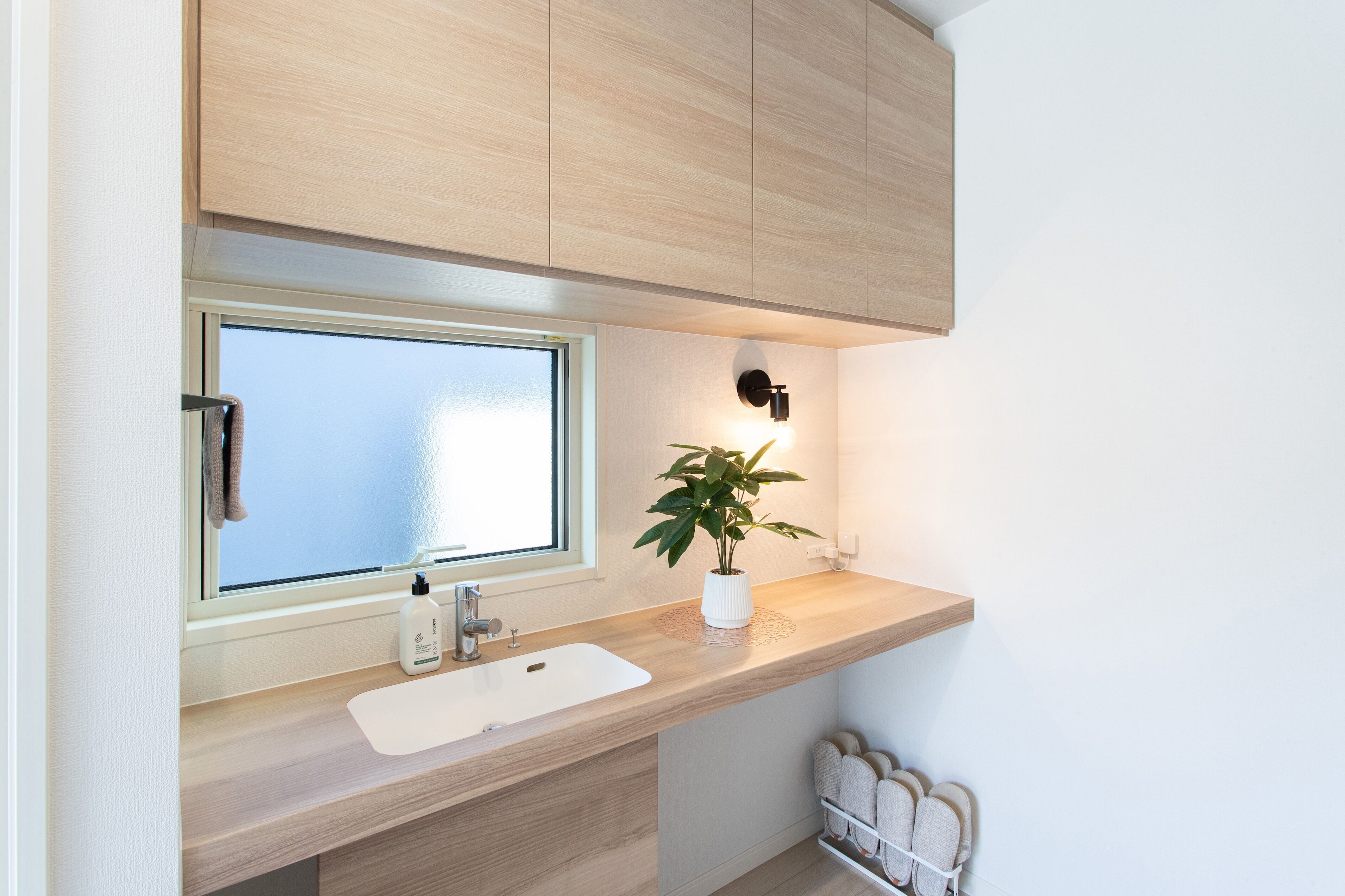 A modern bathroom with a wooden vanity, a window, a sink, a plant, and a towel rack.