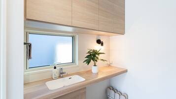 A modern bathroom with a wooden vanity, a window, a sink, a plant, and a towel rack.