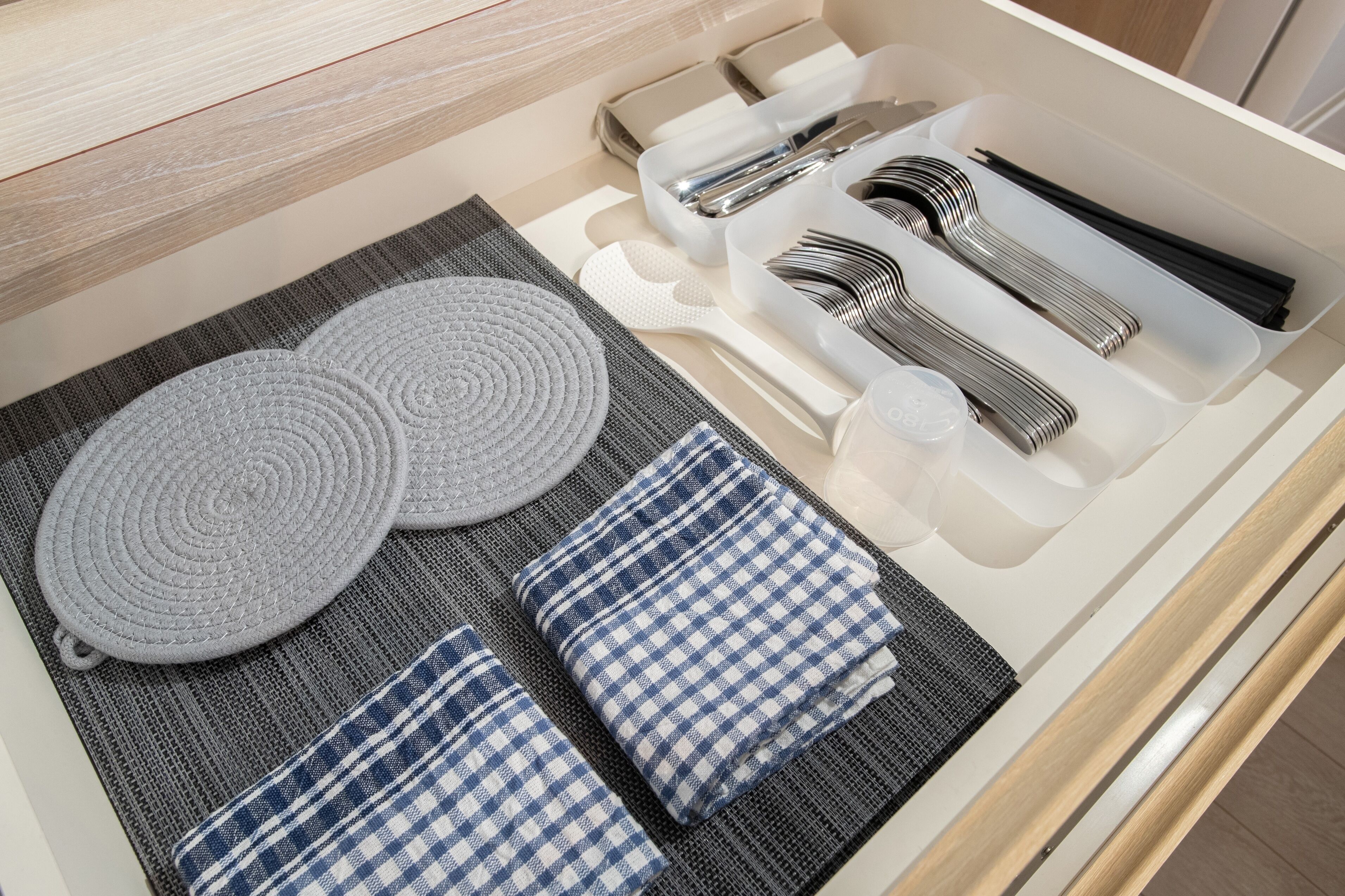A neatly organized drawer with kitchen utensils, two woven placemats, and folded napkins.
