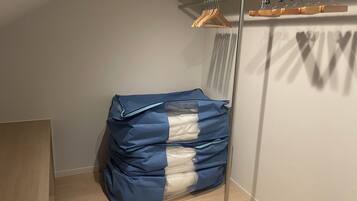 A corner of a room with a metal rack holding wooden hangers, a stack of folded clothes covered with blue and white plastic, and a wooden door frame.