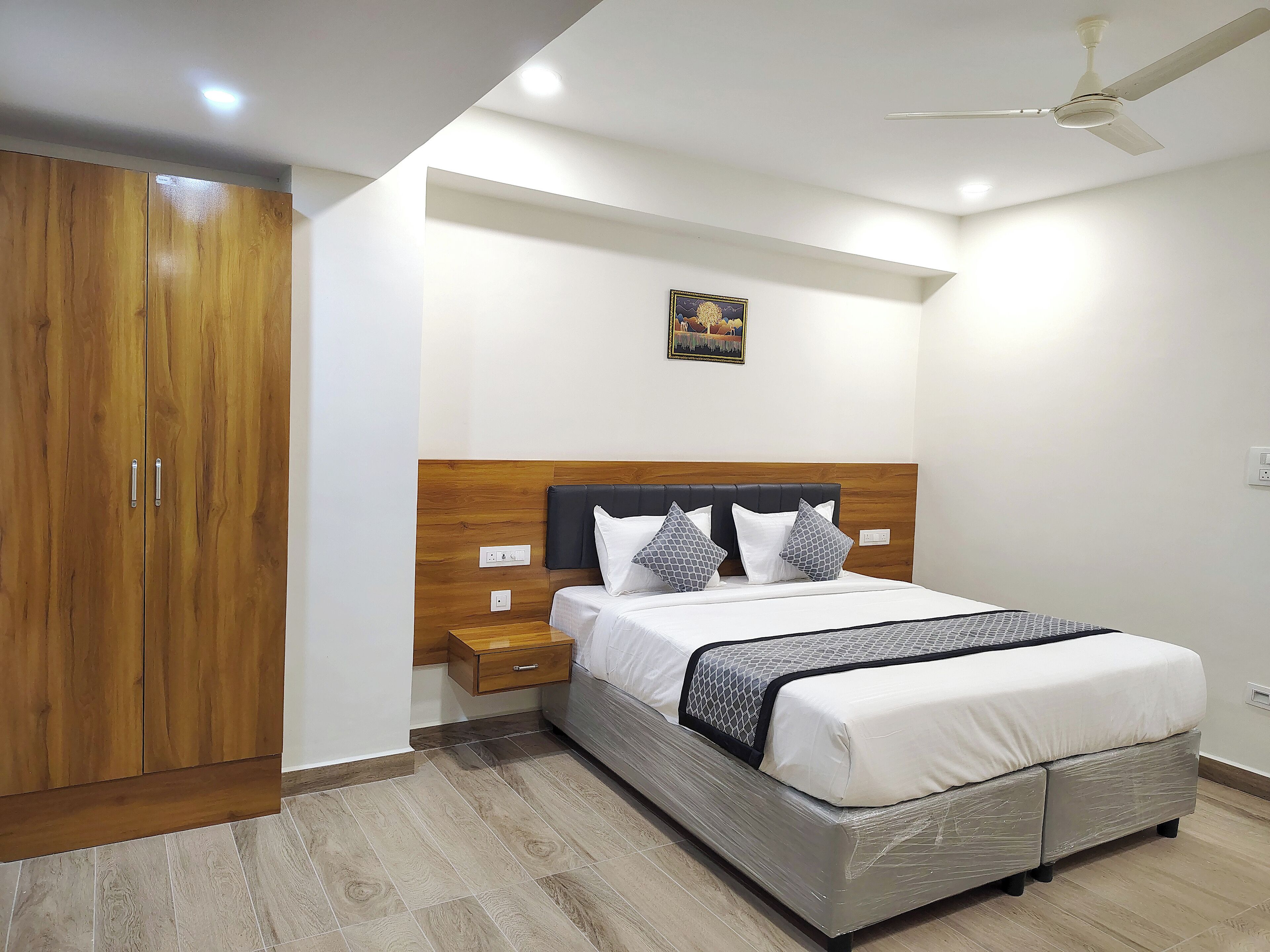 A bedroom with a wooden wardrobe, a bed with a headboard, a nightstand, and a ceiling fan.