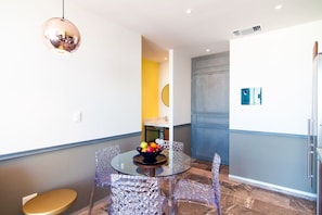 A compact living space with a round glass table, clear chairs, a small round table with fruit, and a modern pendant light.