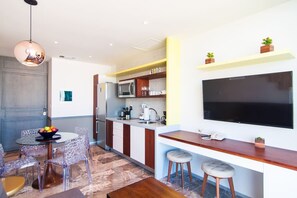 Een moderne keuken met een grote televisie, een eethoek met transparante stoelen, en een bar voorzien van krukken.