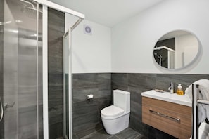 A modern bathroom with a glass-enclosed shower, a white toilet, a vanity with a mirror, and a towel rack. - Mt Roy Delight (Wānaka)