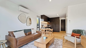 A modern living room with a brown leather sofa, a wooden coffee table, and a dining area with a wooden table and chairs. - Mt Roy Delight (Wānaka)