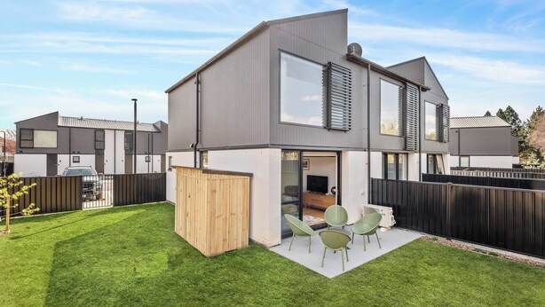 A modern two-story house with a flat roof, a large sliding glass door entrance, and a small patio area with outdoor seating. - Mt Roy Delight (Wānaka)