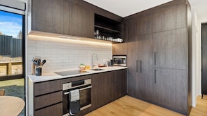 A modern kitchen with dark wood cabinets, a white tiled backsplash, stainless steel appliances, and a wooden dining table. - Mt Roy Delight (Wānaka)