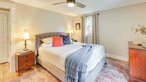 Un dormitorio con cama, mesitas de noche, ventilador de techo y una mesita auxiliar.