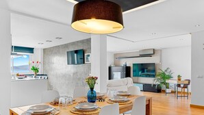 Un comedor moderno con una mesa de madera dispuesta para cuatro personas, una lámpara colgante grande y vistas de la cocina y el área de estar al fondo.