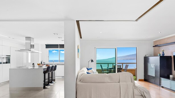 Una cocina moderna con una isla central, un comedor con vista al mar y un espacio de sala de estar acogedor con un ventanal grande.