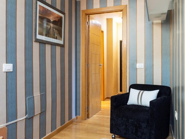 A hallway with striped wallpaper, a framed picture on the wall, a wooden door, and a black armchair with a white pillow. - Rooftop Cityview Classic Suite (Santa Cruz de Tenerife)