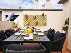 A dining area with a table set for four, surrounded by wicker chairs, and a backdrop of a wall-mounted plant display. - Rooftop Cityview Classic Suite (Santa Cruz de Tenerife)