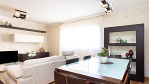 A modern living room with a sofa, a TV, a dining table with chairs, and a kitchen area with shelves. - Rooftop Cityview Classic Suite (Santa Cruz de Tenerife)