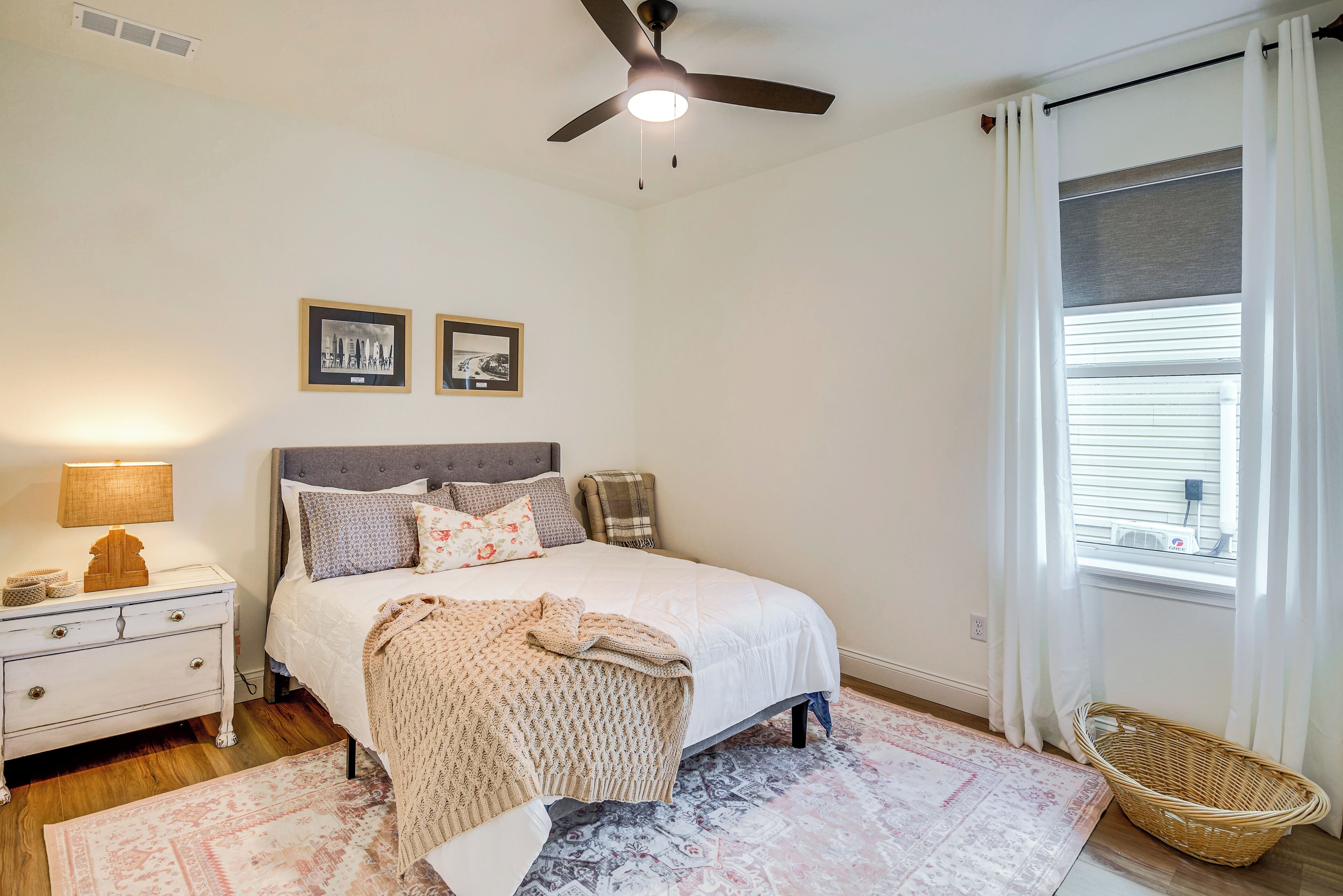 A bedroom with a bed, nightstand, lamp, ceiling fan, and a window with curtains.