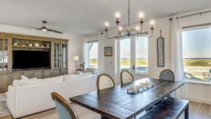 A dining area with a wooden table, chairs, and a television in a room with a view of the beach. - Oceanfront Flagler Beach Unit w/ Water Views! (Flagler Beach)