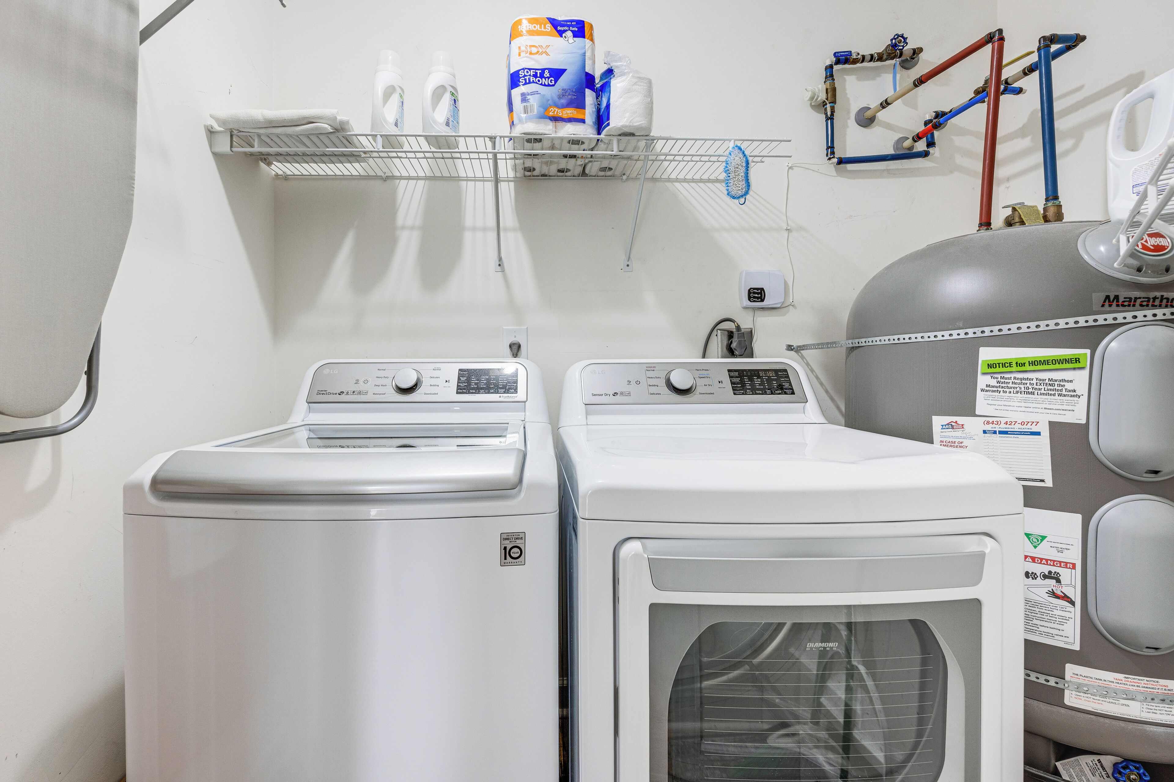 A laundry area with two front-loading washers and a dryer, a shelf with cleaning supplies, and a water heater.