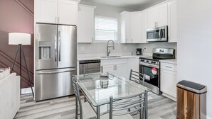 A modern kitchen with white cabinets, stainless steel appliances, a glass dining table, and a trash bin. - < 2 Mi to Jackson Square: New Orleans Home w/ Yard (New Orleans)