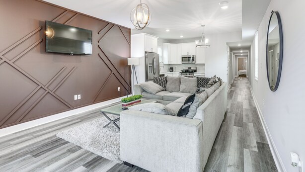 A modern living room with a sofa, a flat-screen TV mounted on a wall, and a kitchen area in the background. - < 2 Mi to Jackson Square: New Orleans Home w/ Yard (New Orleans)