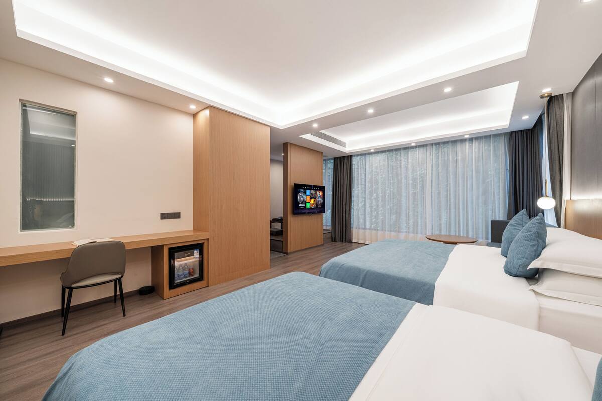 Quarto de hotel com duas camas, uma escrivaninha, televisão e janela.