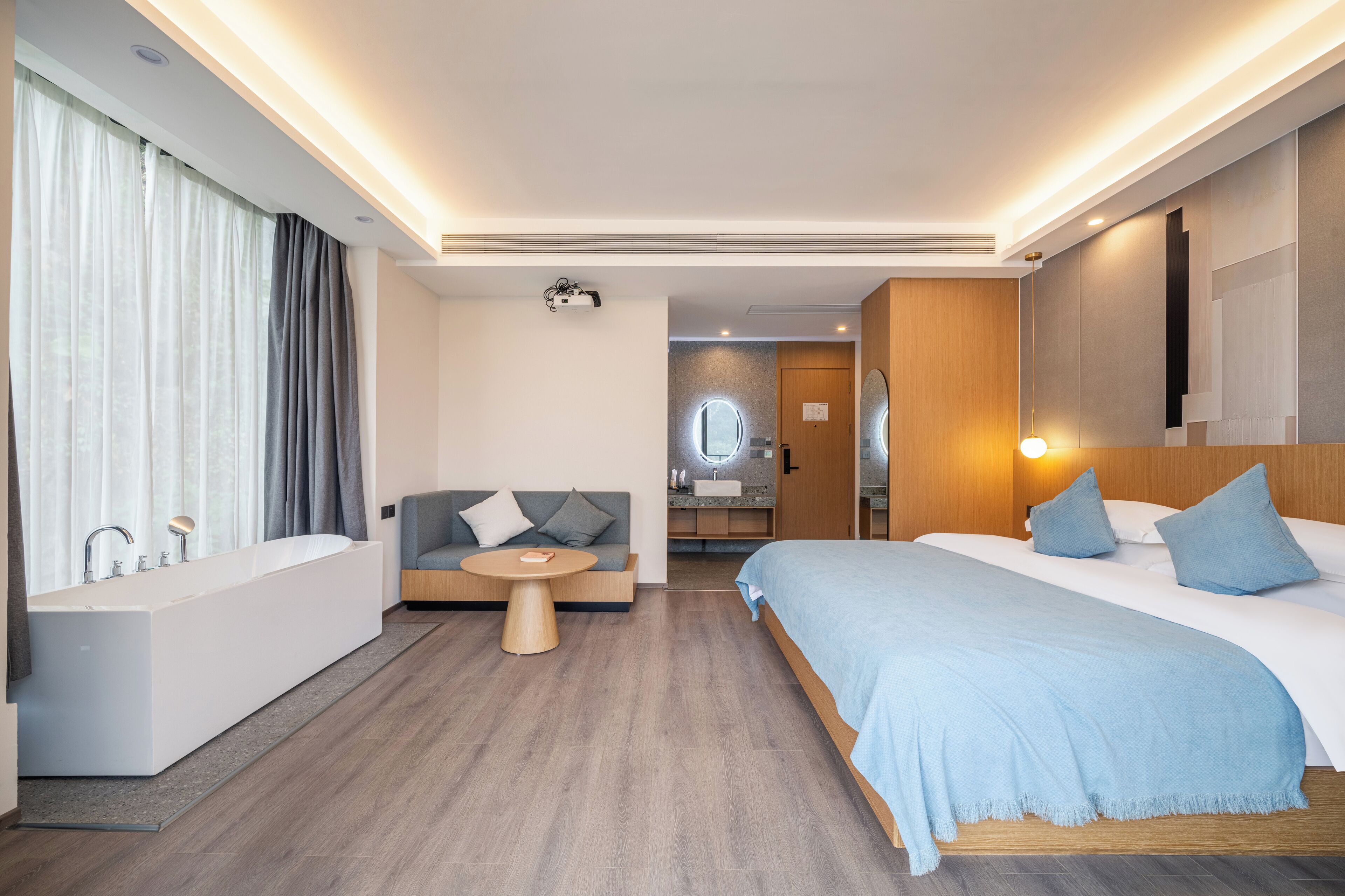 A modern hotel room with a large bed, a separate bathroom, a seating area, and a view of the kitchen.