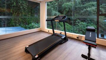 A modern gym with a treadmill, bench, and large windows offering a view of a forested area.