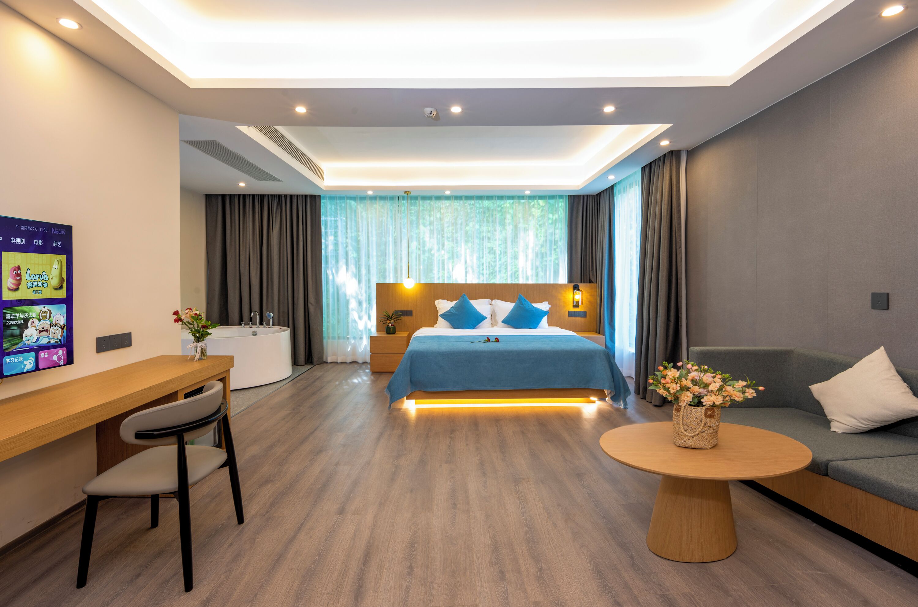 Une chambre d’hôtel moderne avec un lit bien fait, un bureau, un canapé et une table basse ronde.
